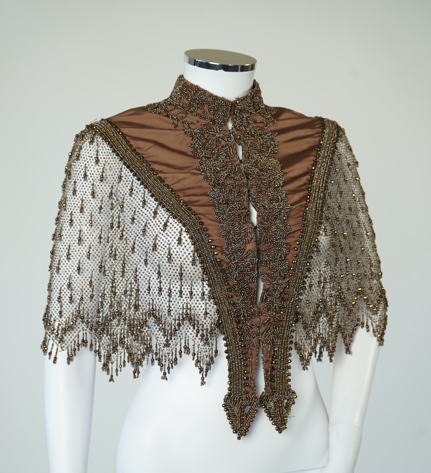 A late 19th century ladies ornate steel and brown beaded and fringed shoulder cape. Made as three ribbed silk panels with ornate beaded appliqués with a beaded and fringed net sleeved cape. Top of neck to bottom of beadi